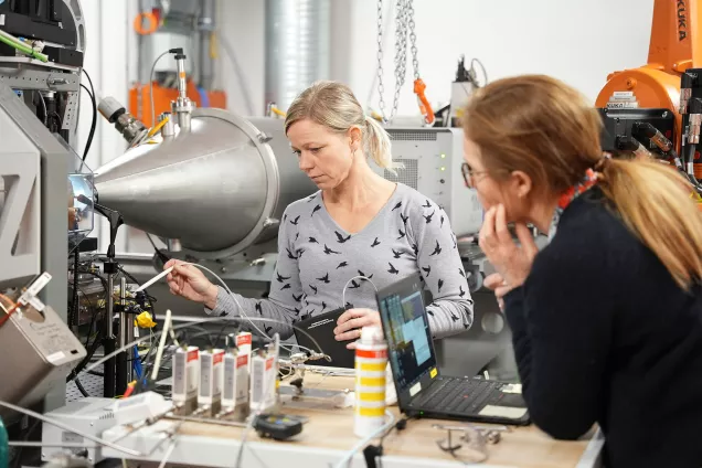 Två kvinnliga forskare diskuterar en teknisk uppställning i ett laboratorium med många avancerade instrument. Foto.