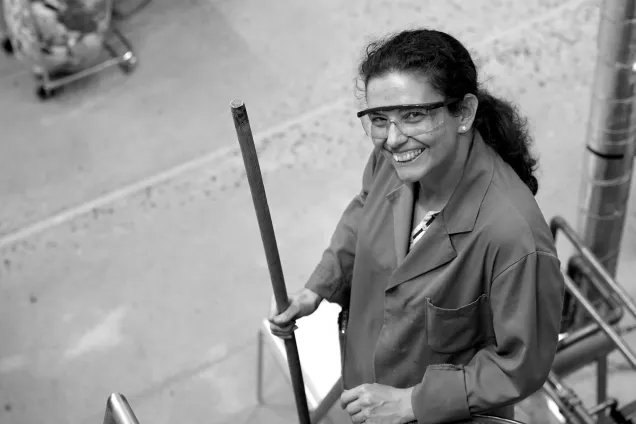 Kvinna i labbrock tittar uppåt i kameran medan hon håller i en pinne. Foto.