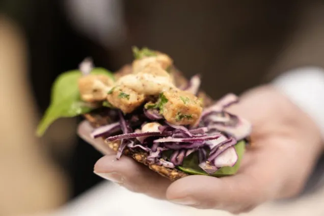 Hand som håller ett knäckebröd med vegetariskt pålägg. Foto.